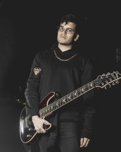 Foto de guitarrista de la banda ground of chaos sostienendo una guitarra en la noche con ropa negra