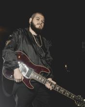 Foto de guitarrista de la banda ground of chaos sostienendo una guitarra en la noche con ropa negra